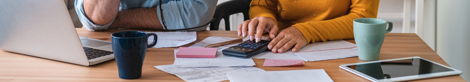 People using a calculator at a table with coffee cups and papers