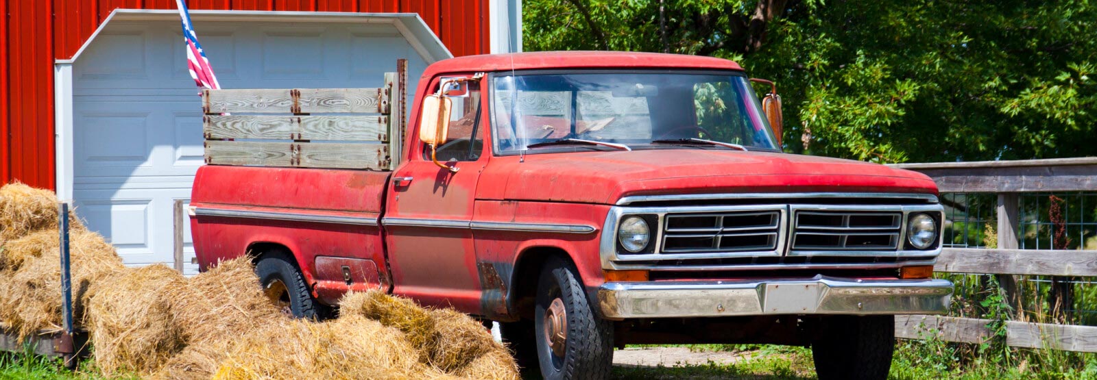 An old red farm truck with an American flag in the background